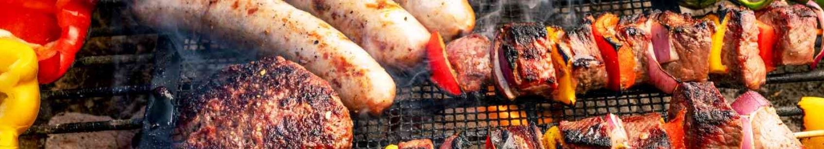 Grilling barbecue with sausage, steak, and skewered peppers and onions over charcoal.