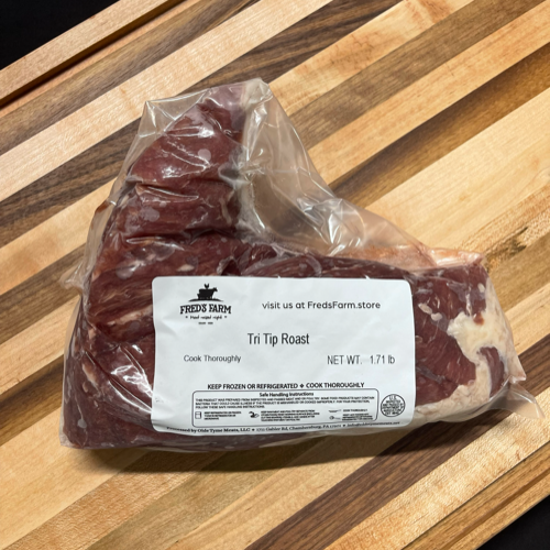 Vacuum-sealed tri-tip roast labeled Fred's Farm, 1.71 lb, resting on a wooden cutting board. The meat is marbled with fat and covered in clear plastic wrap.