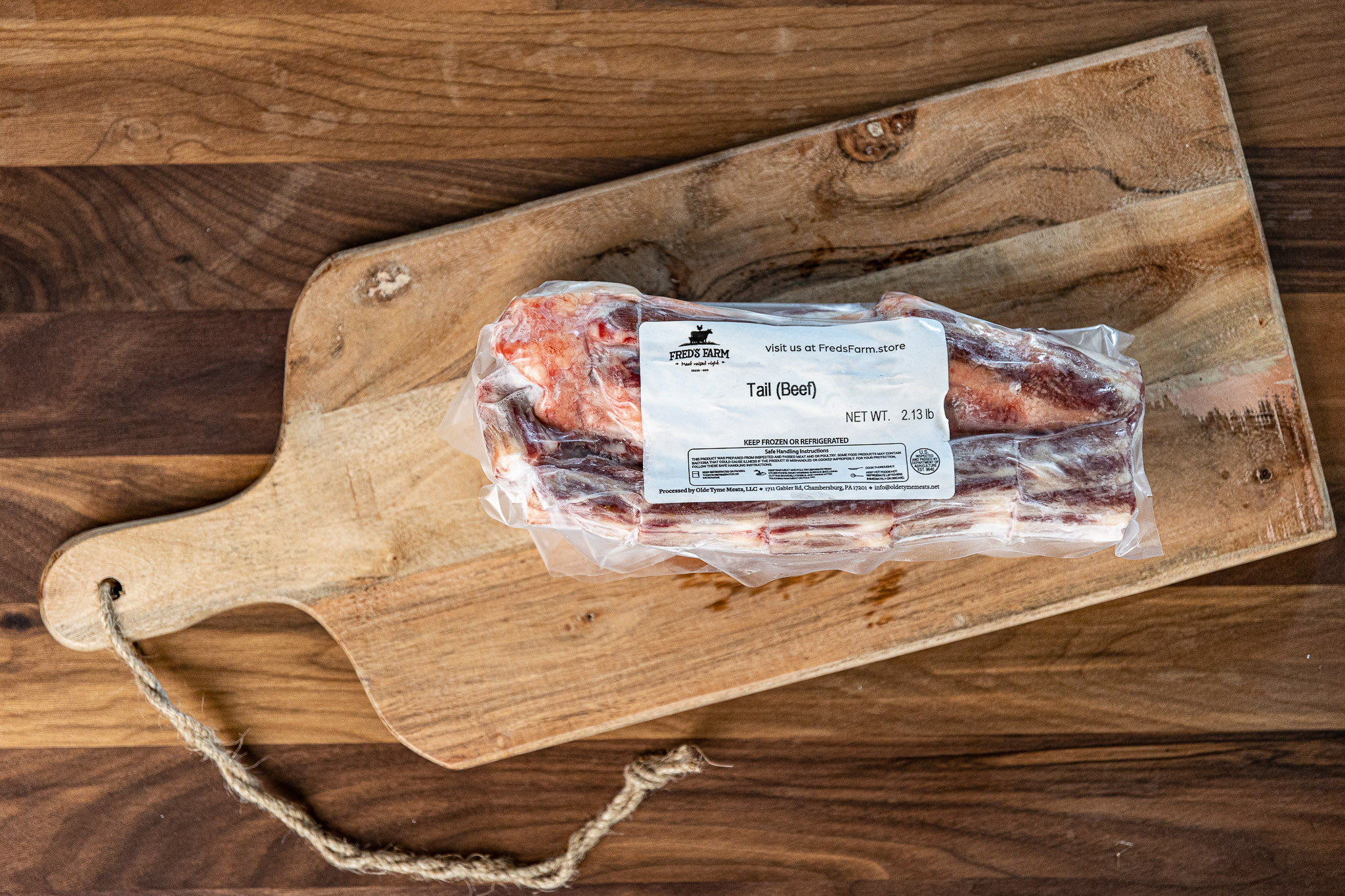 Beef tail package in plastic wrap on a wooden cutting board; label reads Tail (Beef) and shows Fred's Farm branding.