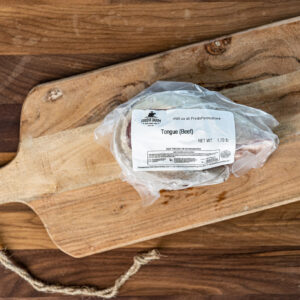 Beef tongue in a plastic bag on a wooden cutting board with a label that reads 'Tongue (Beef)'.
