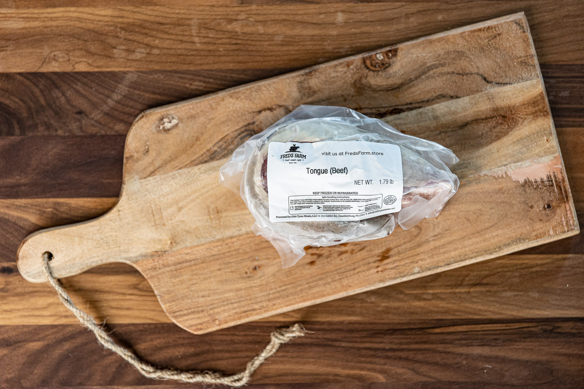 Beef tongue in a plastic bag on a wooden cutting board with a label that reads 'Tongue (Beef)'.
