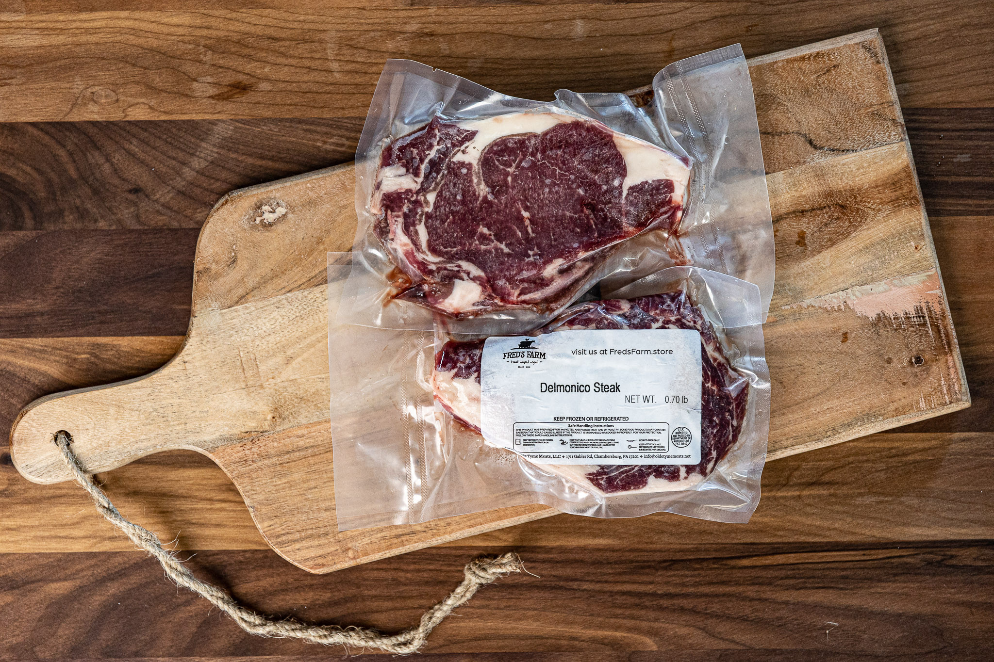 Vacuum-sealed Delmonico steak on a wooden cutting board, label reads 'Delmonico Steak' from Fred's Farm; raw beef.