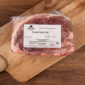 Vacuum-sealed pork shoulder roast on a wooden cutting board with a label reading 'Shoulder Roast (Pork)'.