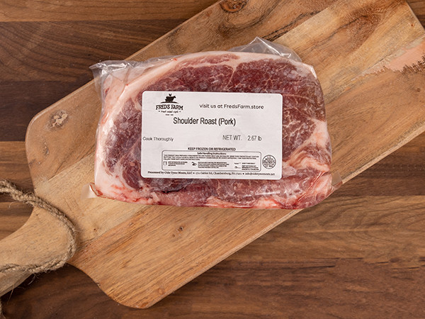 Vacuum-sealed pork shoulder roast on a wooden cutting board with a label reading 'Shoulder Roast (Pork)'.