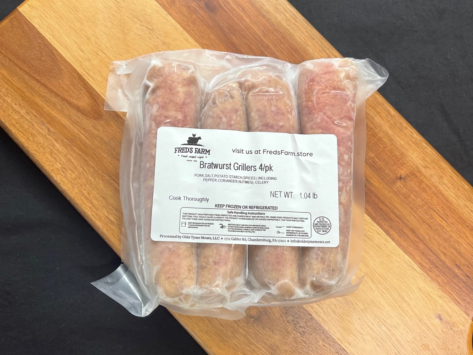 Pack of four bratwurst sausages in vacuum-sealed plastic with a Fred's Farm label on a wood surface.