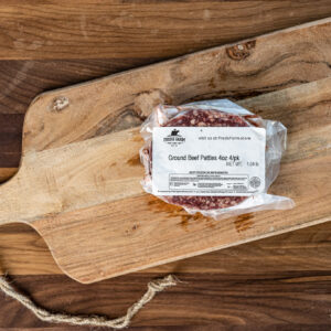 Vacuum-sealed package of ground beef patties on a rustic wooden cutting board.