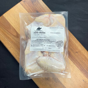 Vacuum-sealed bag of chicken wings on a wooden board, labeled Fred's Farm (keep refrigerated).