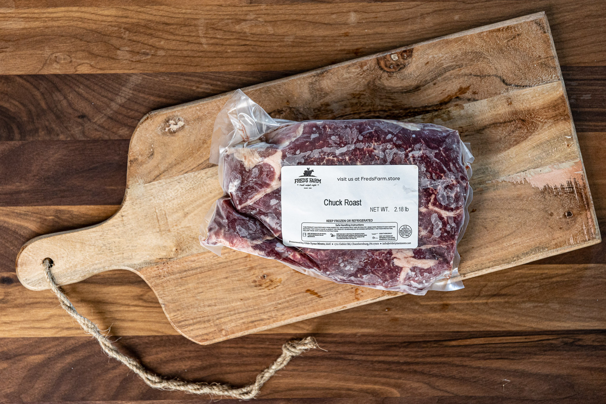 Vacuum-sealed chuck roast on a wooden cutting board with a label reading 'Chuck Roast' from Fred's Farm store -- meat packaging on rustic table surface.