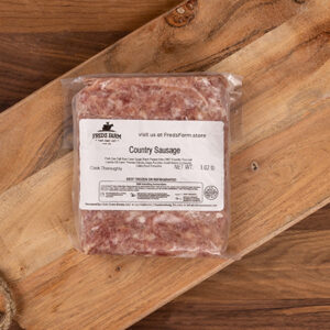 Vacuum-sealed country sausage on a wooden cutting board with a label from Fred's Farm, Frozen product.