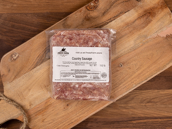 Vacuum-sealed country sausage on a wooden cutting board with a label from Fred's Farm, Frozen product.