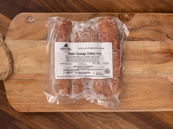 Vacuum-sealed bag containing four maple sausage grillers on a wooden cutting board with a label reading 'Maple Sausage Grillers 4 pk'