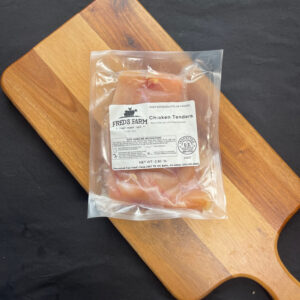 Vacuum-sealed bag of chicken tenders labeled Fred's Farm on a wooden cutting board.