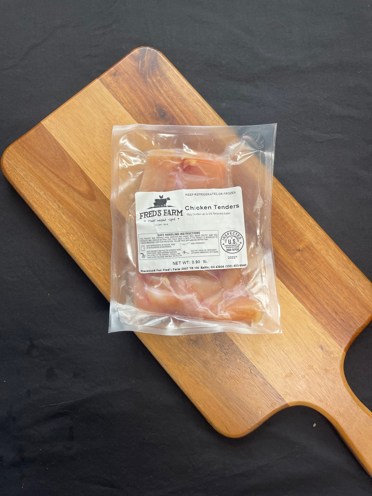 Vacuum-sealed bag of chicken tenders labeled Fred's Farm on a wooden cutting board.