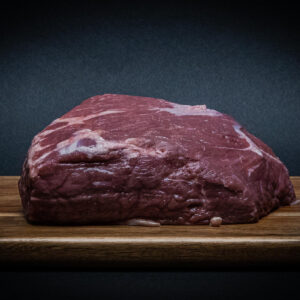 Thick raw beef steak with visible marbling on a wooden cutting board against a dark background.