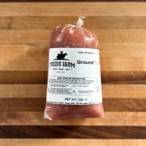 Ground sausage in red casing with Fred's Farm label resting on a wooden cutting board.