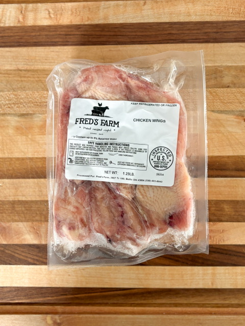Vacuum-sealed bag of frozen chicken wings labeled Fred's Farm, weighing about 1.23 lb, placed on a wooden surface.