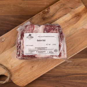 Frozen Boston butt pork roast in a vacuum-sealed bag on a wooden cutting board, label visible on the package.