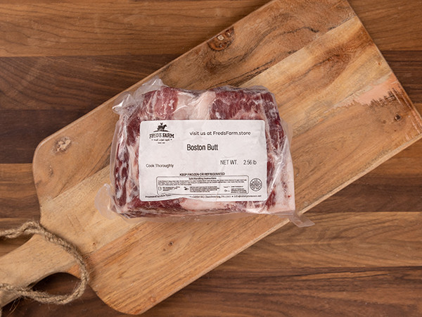 Frozen Boston butt pork roast in a vacuum-sealed bag on a wooden cutting board, label visible on the package.