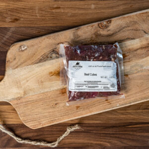 Vacuum-sealed package labeled Beef Cubes on a wooden cutting board with a rope background.