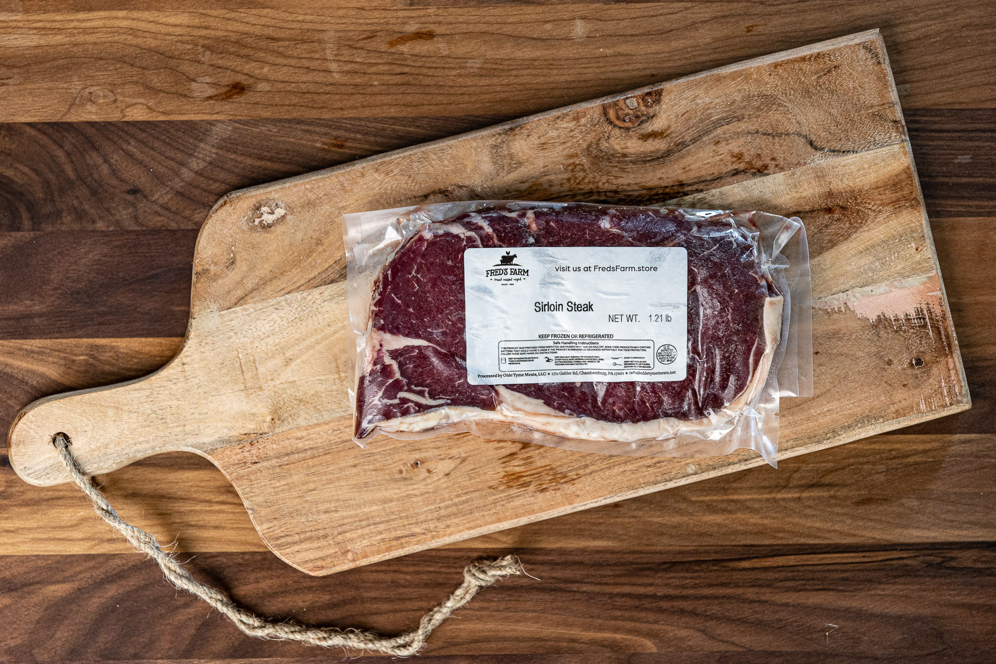 Vacuum-sealed sirloin steak on a rustic wooden cutting board with a rope handle nearby.