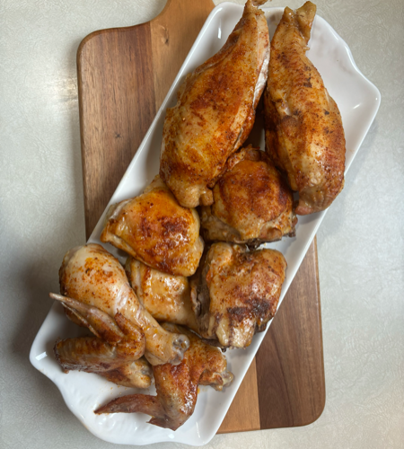 Plate of roasted chicken wings with crispy brown skin arranged on a white platter over a wooden board