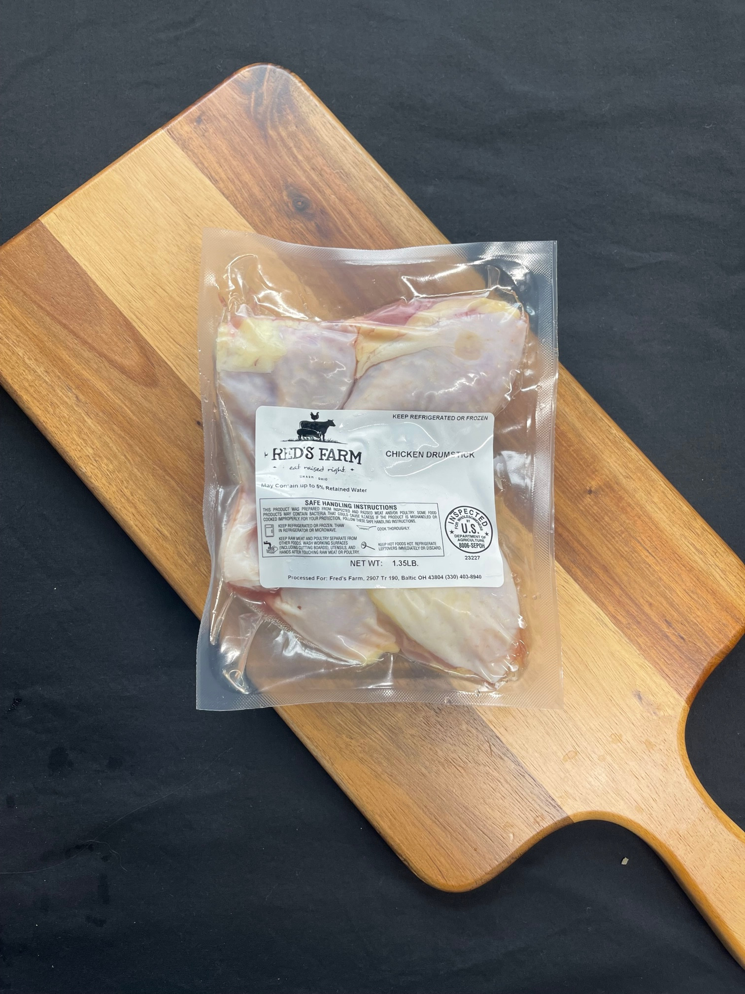 Vacuum-sealed chicken drumsticks on a wooden cutting board with a Fred's Farm label visible.