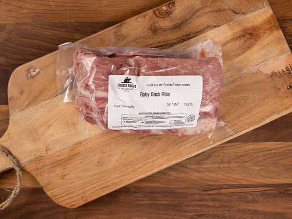 Vacuum-sealed Baby Back Ribs on a wooden cutting board with a label showing Fred's Farm.