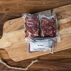 Two vacuum-sealed filet mignon steaks on a wooden cutting board.