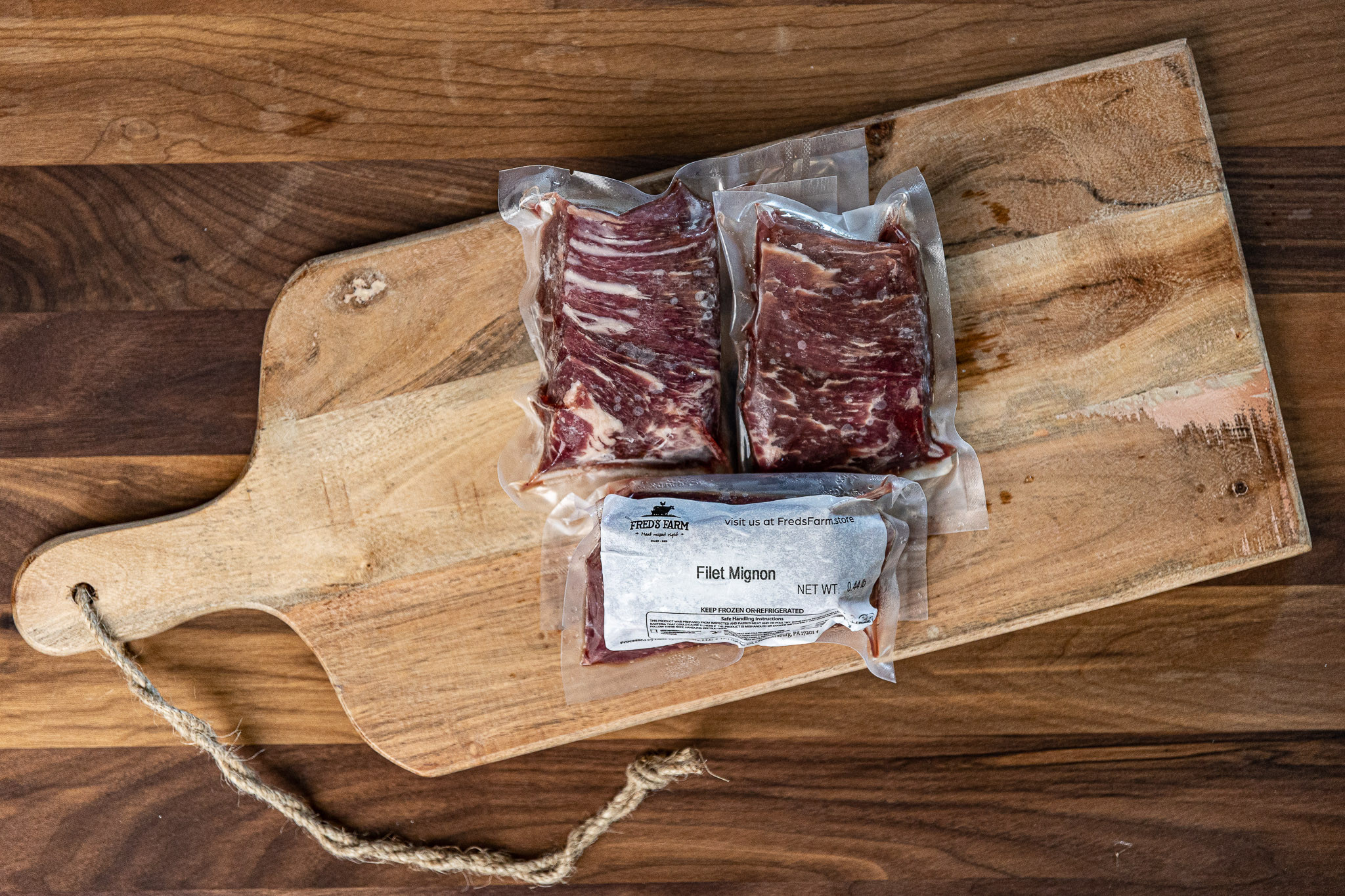 Two vacuum-sealed filet mignon steaks on a wooden cutting board.