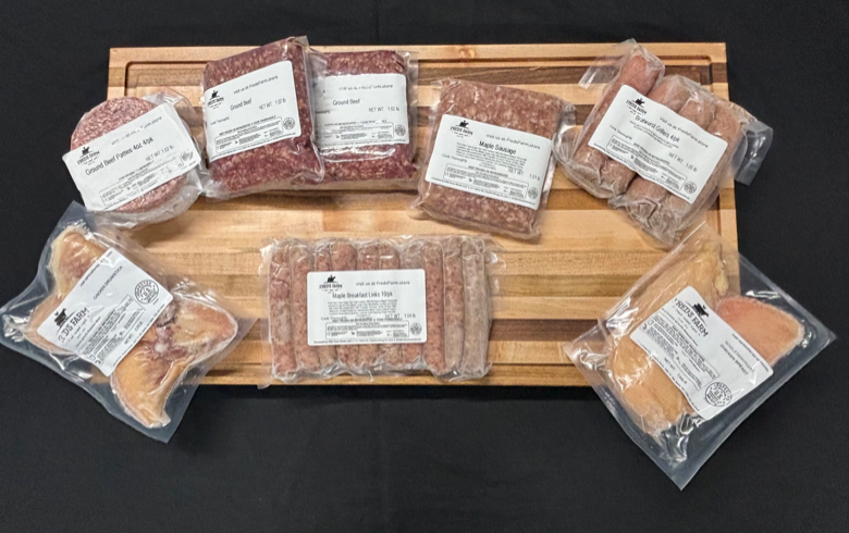 Assorted vacuum-sealed meat packages (sausages and burgers) arranged on a wooden cutting board.