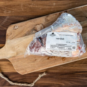 Vacuum-sealed beef heart with a label reading 'Heart (Beef)' on a wooden cutting board.