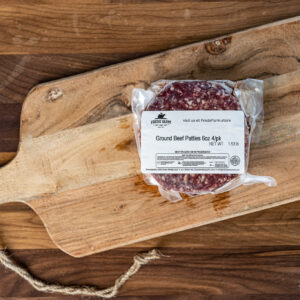 Vacuum-sealed package of ground beef patties on a rustic wooden cutting board with a knotted rope handle nearby.
