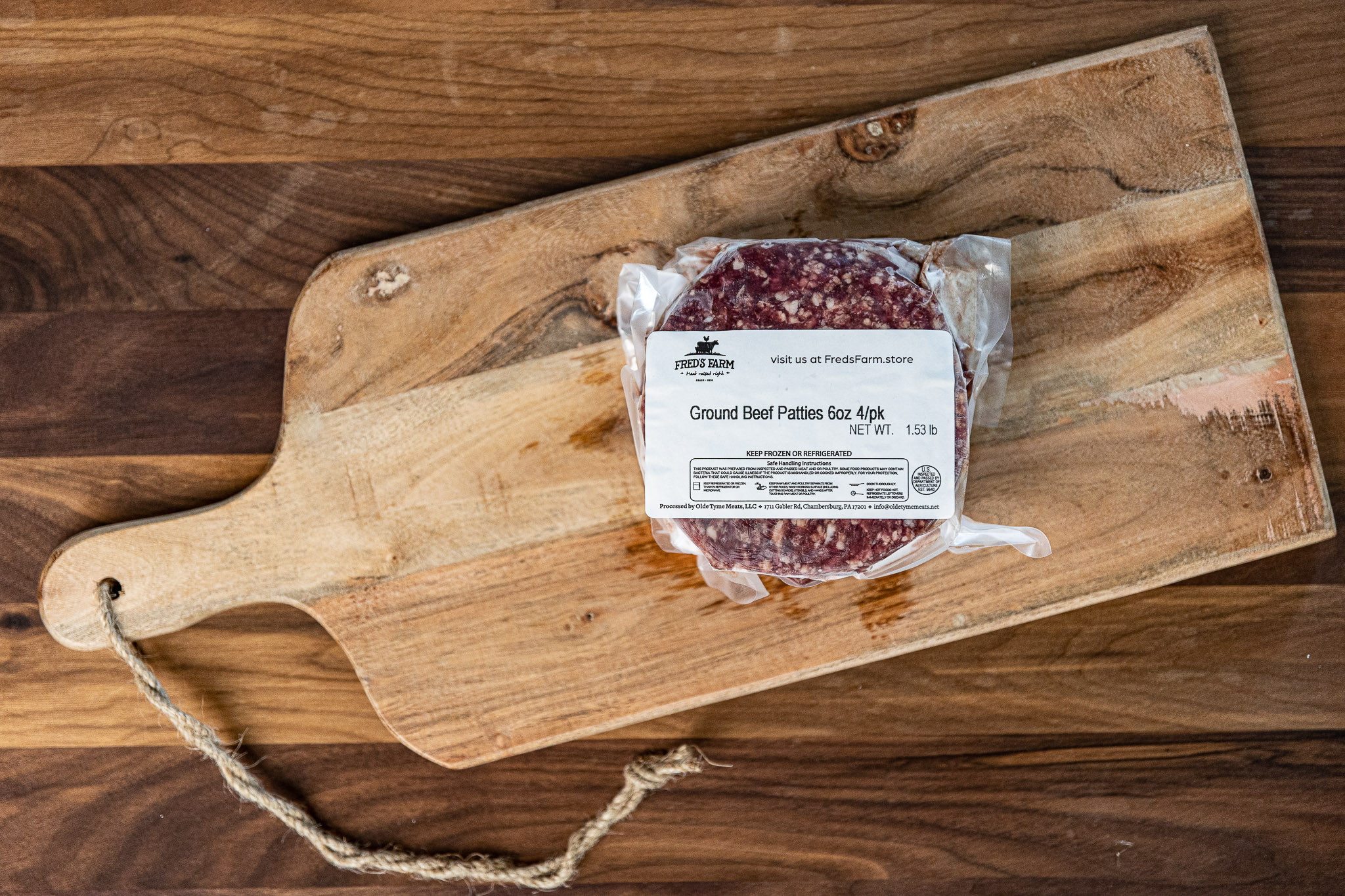 Vacuum-sealed package of ground beef patties on a rustic wooden cutting board with a knotted rope handle nearby.