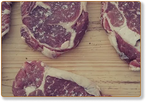 Rectangle 76 - Fred's Farm - Fred's Farm Raw beef steaks arranged on a light wooden cutting board.