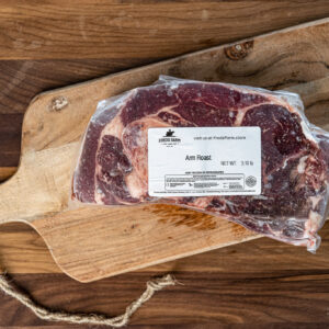 Vacuum-sealed beef roast labeled 'Arm Roast' on a wooden cutting board with a rope handle nearby.