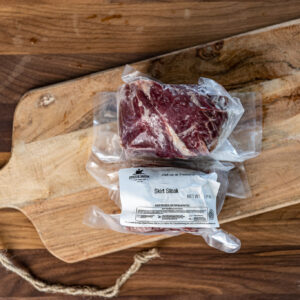 Vacuum-sealed skirt steak on a wooden cutting board with a plastic bag and printed label visible at the bottom edge.