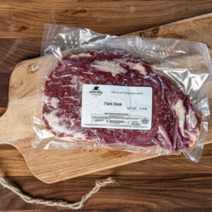 Frozen flank steak in a vacuum-sealed bag on a wooden cutting board with a label from Fred's Farm (1.18 lb)