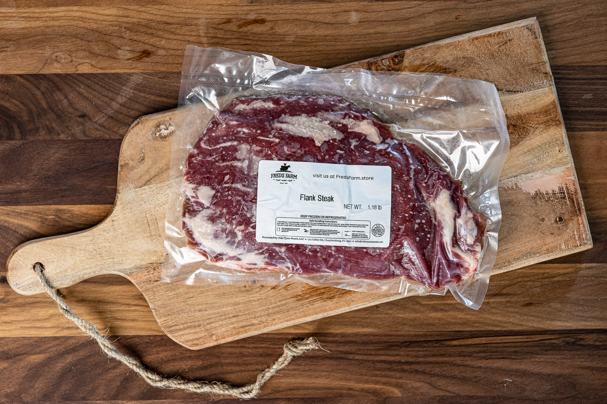 Frozen flank steak in a vacuum-sealed bag on a wooden cutting board with a label from Fred's Farm (1.18 lb)
