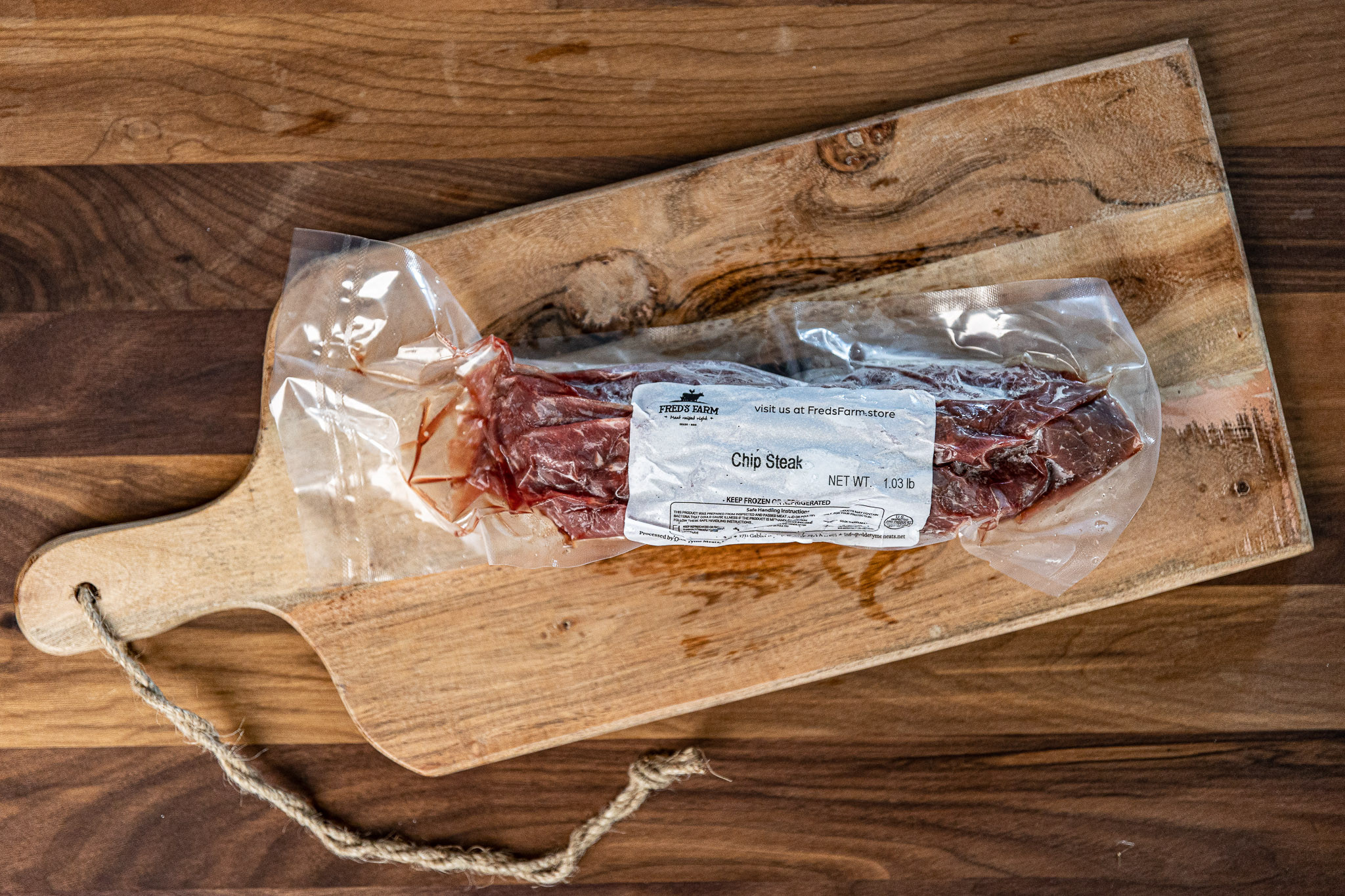 Vacuum-sealed chip steak on a wooden cutting board with a label from Fred's Farm showing net weight 1.03 lb.
