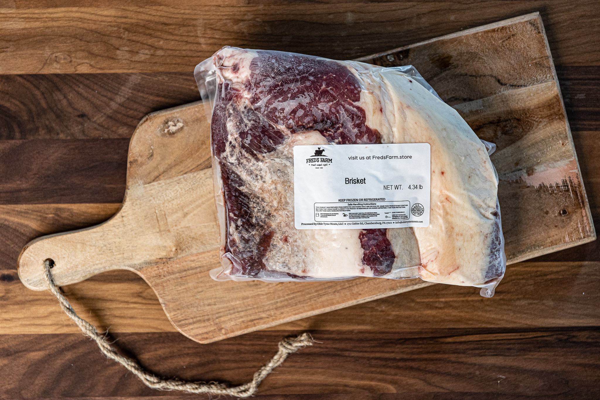 Brisket in plastic wrap on a wooden cutting board with a Fred's Farm label showing it weighs 4.34 lb.