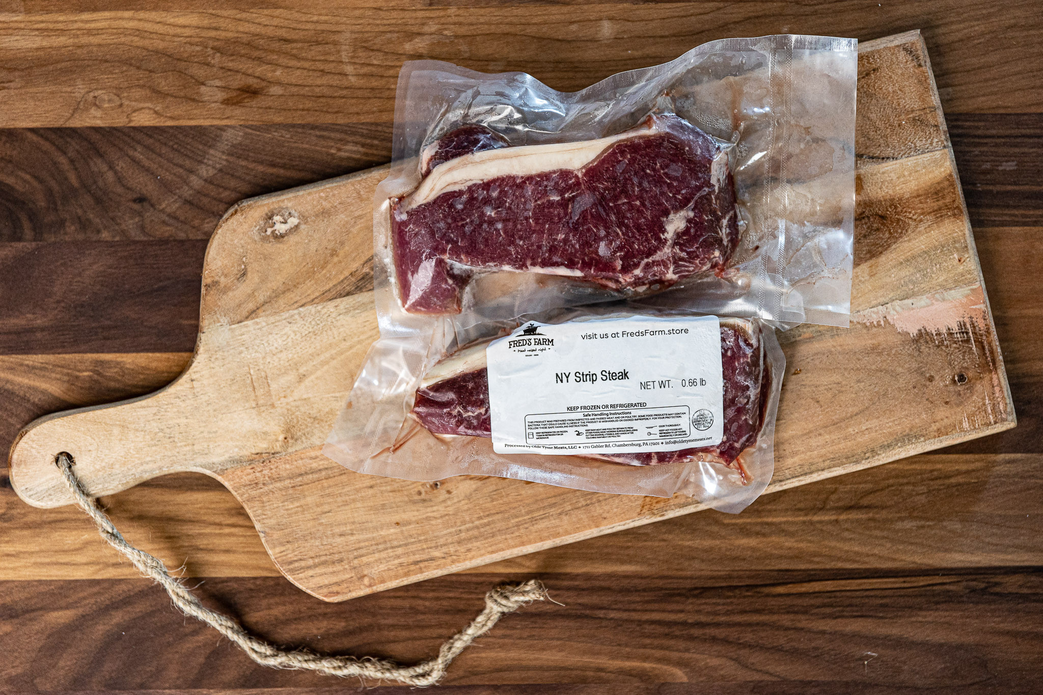 Vacuum-sealed raw NY strip steak on a wooden cutting board with a label reading Fred's Farm.