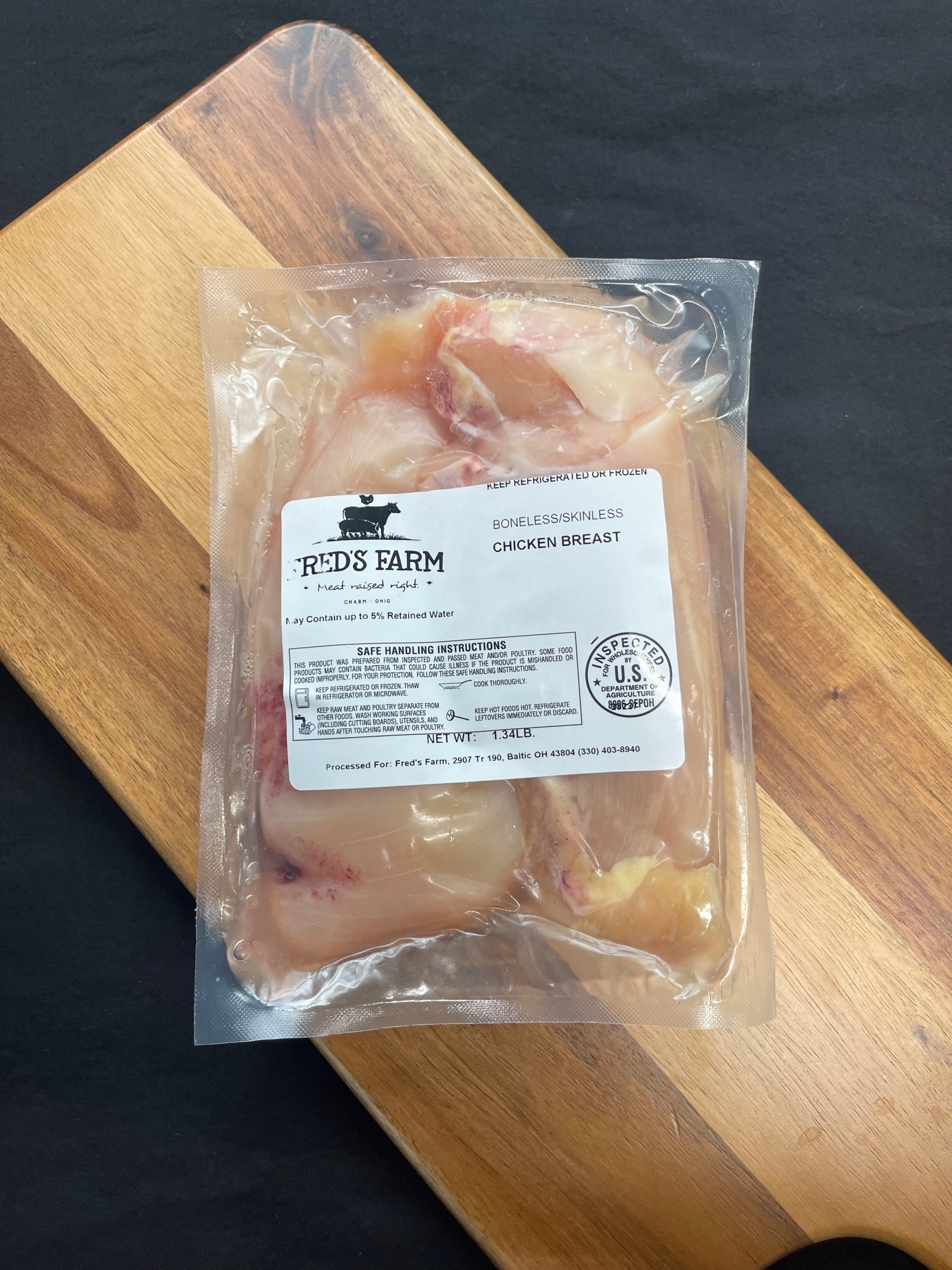 Vacuum-sealed chicken breast from Red's Farm on a wooden cutting board, ready to thaw or cook.