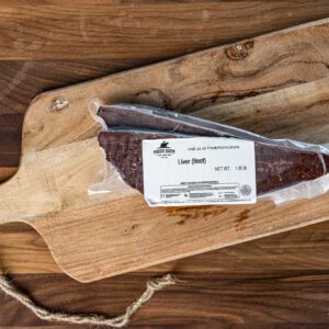 Vacuum-sealed beef liver on a rustic wooden cutting board with a rope handle.
