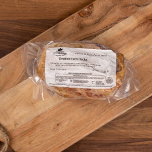 Vacuum-sealed package of smoked ham hocks resting on a wooden cutting board.