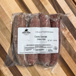 Vacuum-sealed package of four country sausage grillers from Fred's Farm on a wooden cutting board; label shows brand and net weight 0.99 lb.