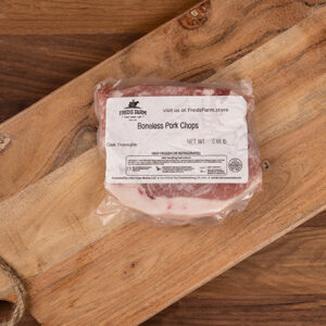 Boneless pork chops in plastic packaging on a wooden cutting board, label visible.