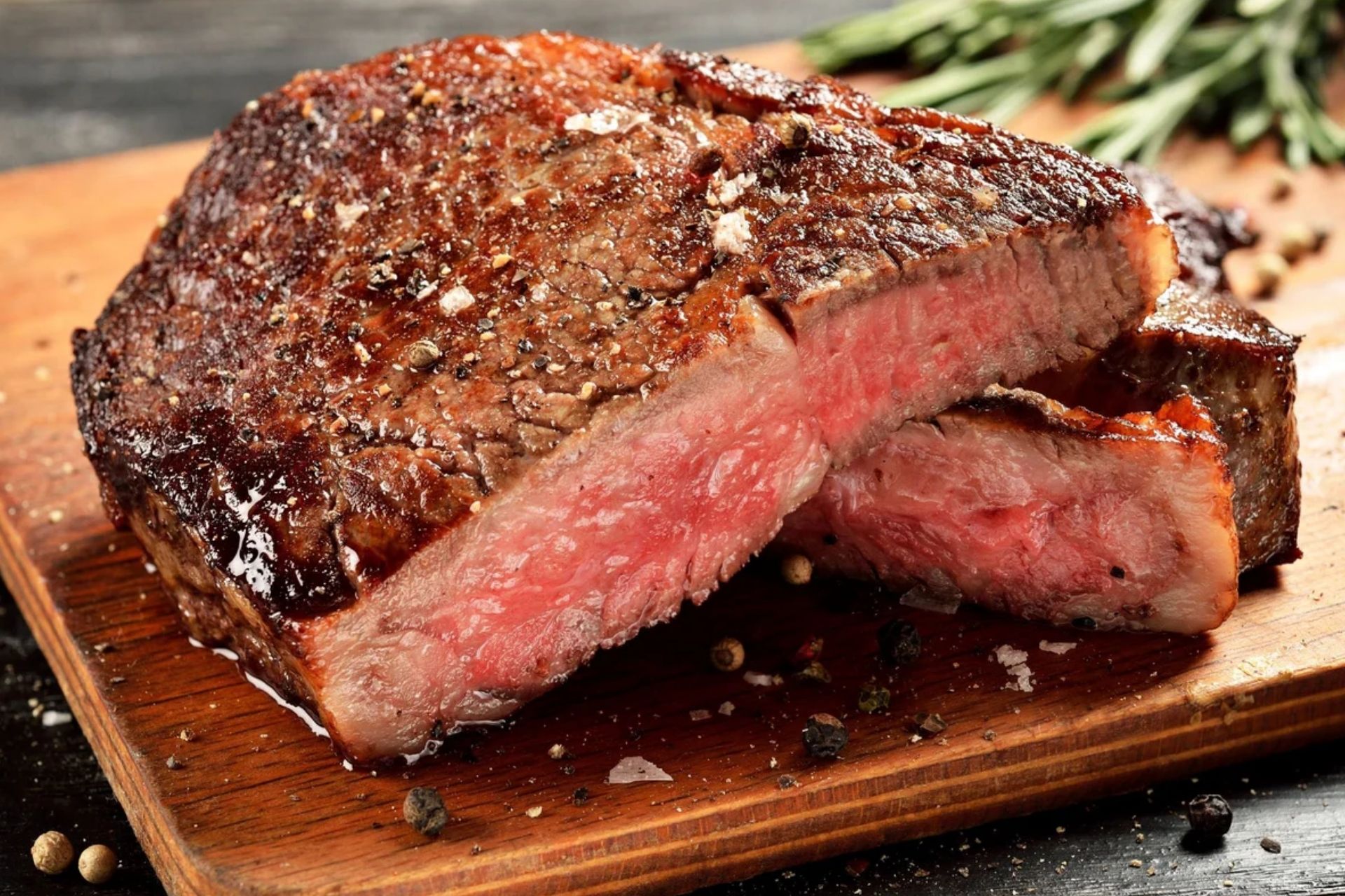 Juicy pepper-crusted beef roast on a wooden cutting board, showing a pink, medium-rare center.