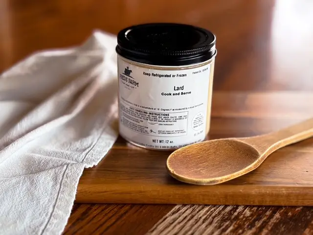 Jar labeled 'Lard – Cook and Serve' with a black lid on a wooden table, beside a wooden spoon and towel, in a kitchen scene.