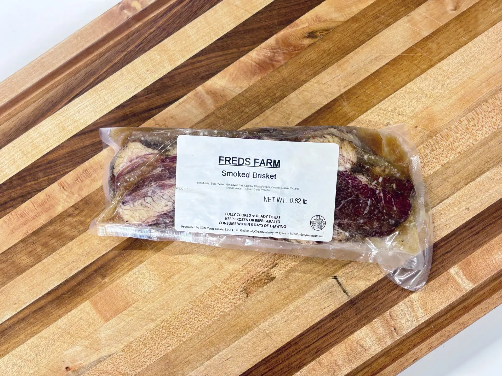 Vacuum-sealed smoked brisket labeled Fred's Farm on a wooden cutting board