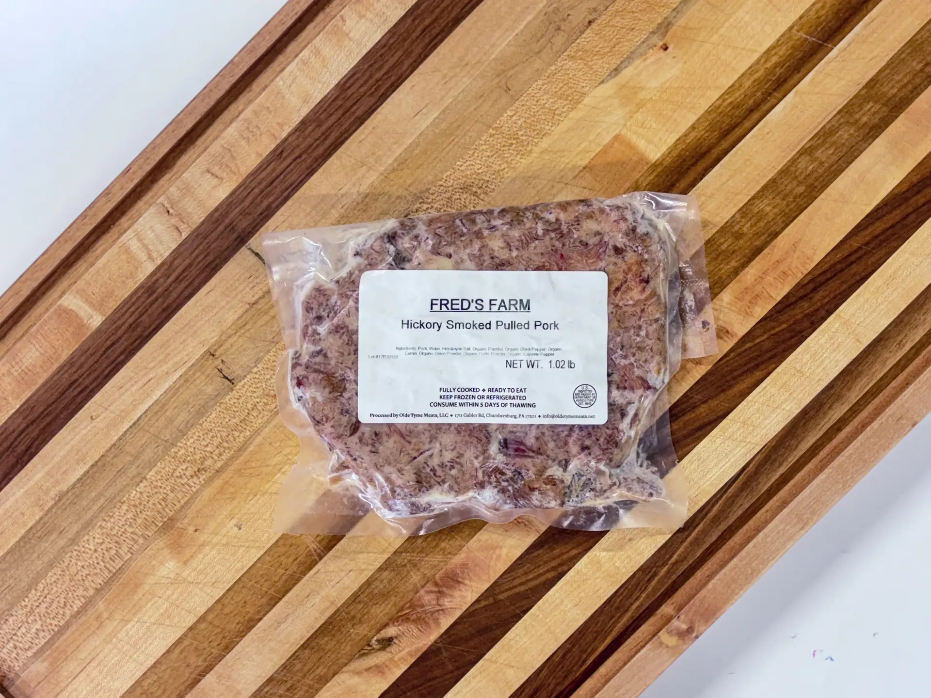 Vacuum-sealed bag of Fred's Farm Hickory Smoked Pulled Pork on a wooden cutting board, labeled and ready to heat or eat.